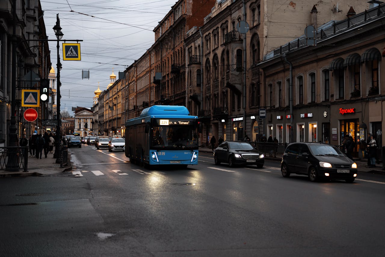 Urban evening street scene with vehicles, a bus, and historic buildings under a cloudy sky.