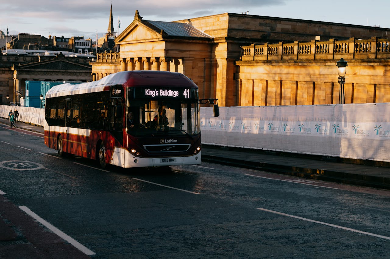 Modern bus driving on asphalt roadway near aged house exteriors and fenced sidewalk in town